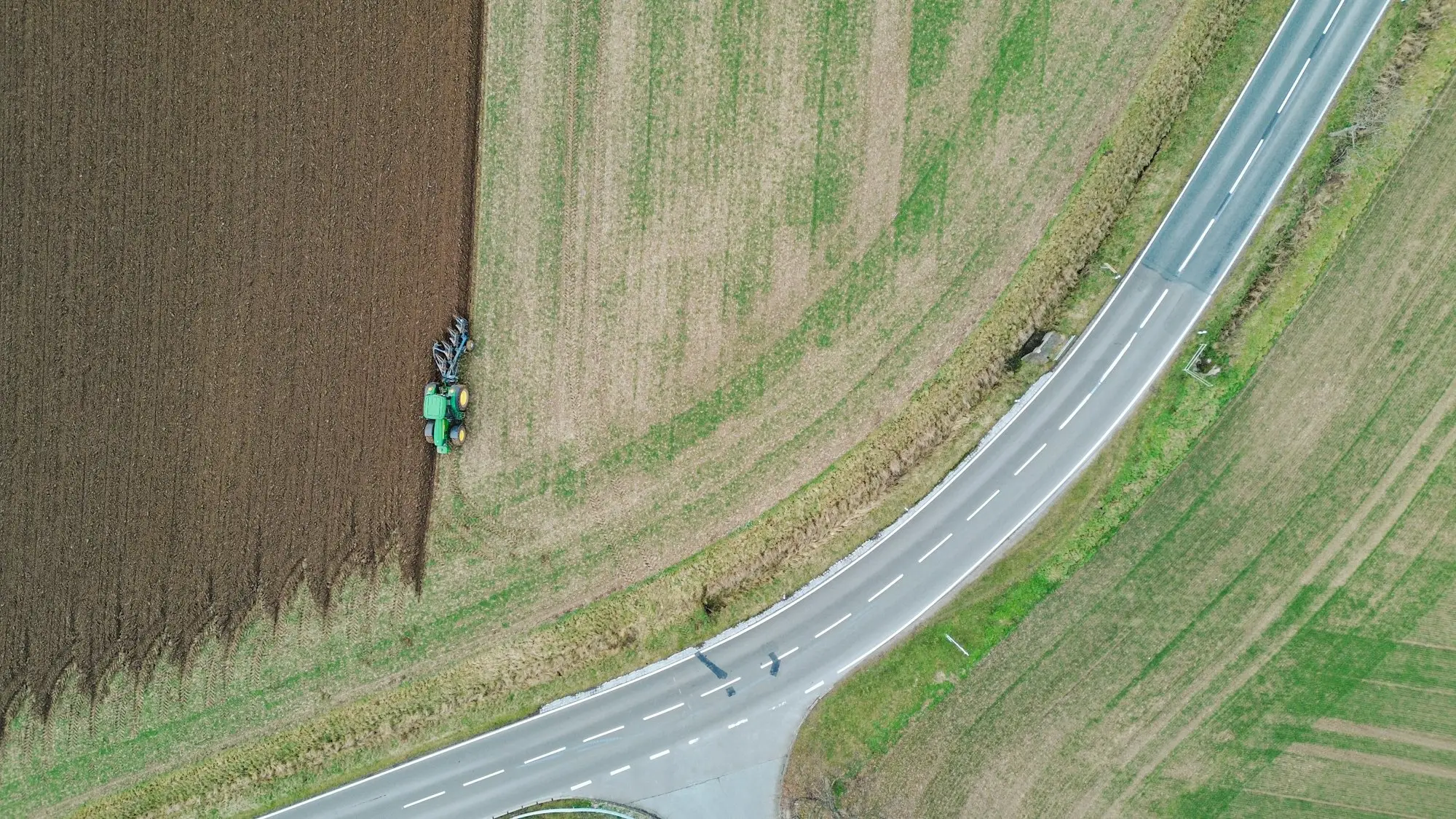 Aerial view of a quiet country road with a tractor working the paddock beside it, a different route to business funding